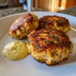 Three golden-brown, crispy salmon cakes garnished with fresh dill, served with a dollop of creamy sauce.