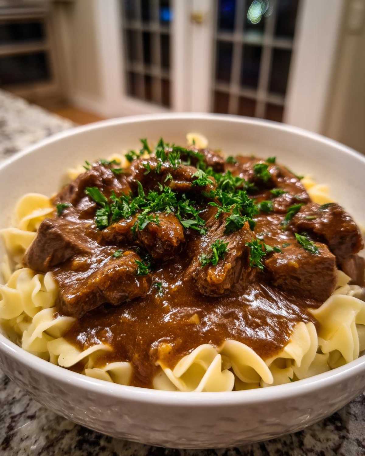 Close-up of tender crockpot beef tips smothered in rich brown gravy served over wide egg noodles and topped with fresh parsley.