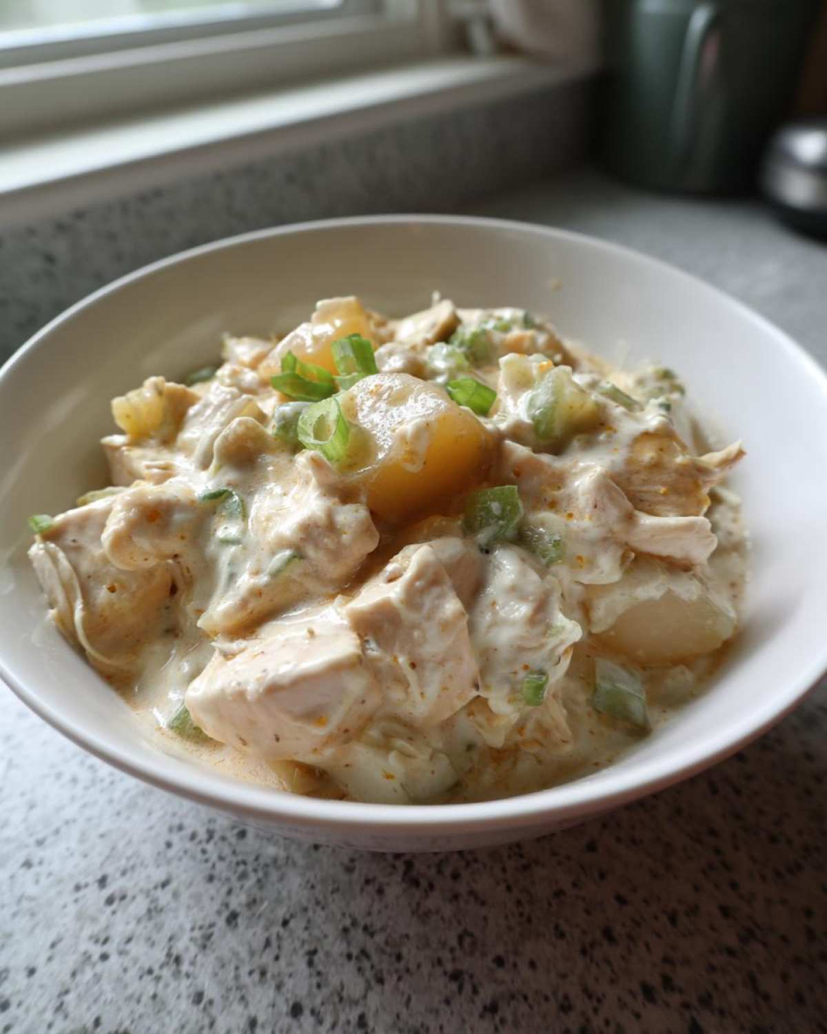 A close-up of a hearty serving of crockpot white chicken chili, featuring chunks of chicken and beans in a creamy sauce, topped with green onions.