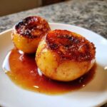 Close-up of two golden baked pears topped with caramelized brown sugar and cinnamon, sitting in a pool of rich sauce.