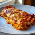 Two baked easy chicken enchiladas covered in bubbling, melted cheese and red sauce on a white plate.