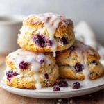 A stack of three flaky blueberry scones drizzled generously with a thick vanilla glaze.