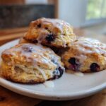 A stack of three flaky blueberry scones topped with a sweet white glaze, ready to eat.