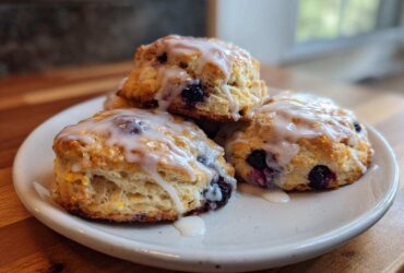 A stack of three flaky blueberry scones topped with a sweet white glaze, ready to eat.