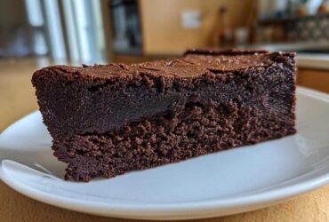 Close-up of a dense, fudgy slice of flourless chocolate cake served on a white plate.