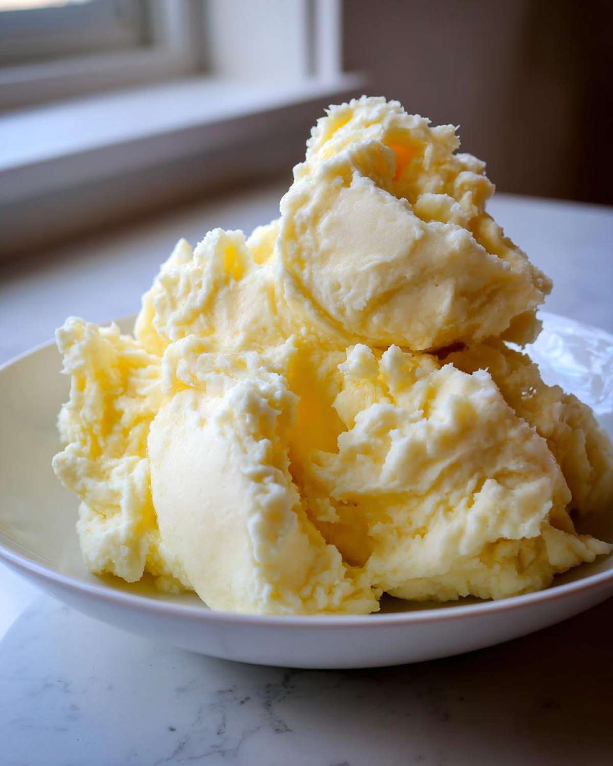 A large, fluffy mound of rich, yellow creamy mashed potatoes served in a white bowl.