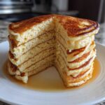 A tall stack of incredibly fluffy pancakes, cut to show the airy interior, drizzled with syrup.