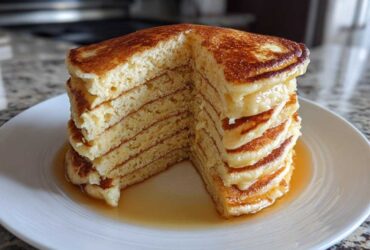 A tall stack of incredibly fluffy pancakes, cut to show the airy interior, drizzled with syrup.
