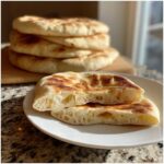 Close-up of fluffy pita bread torn open showing the airy interior texture, with more pita bread stacked in the background.