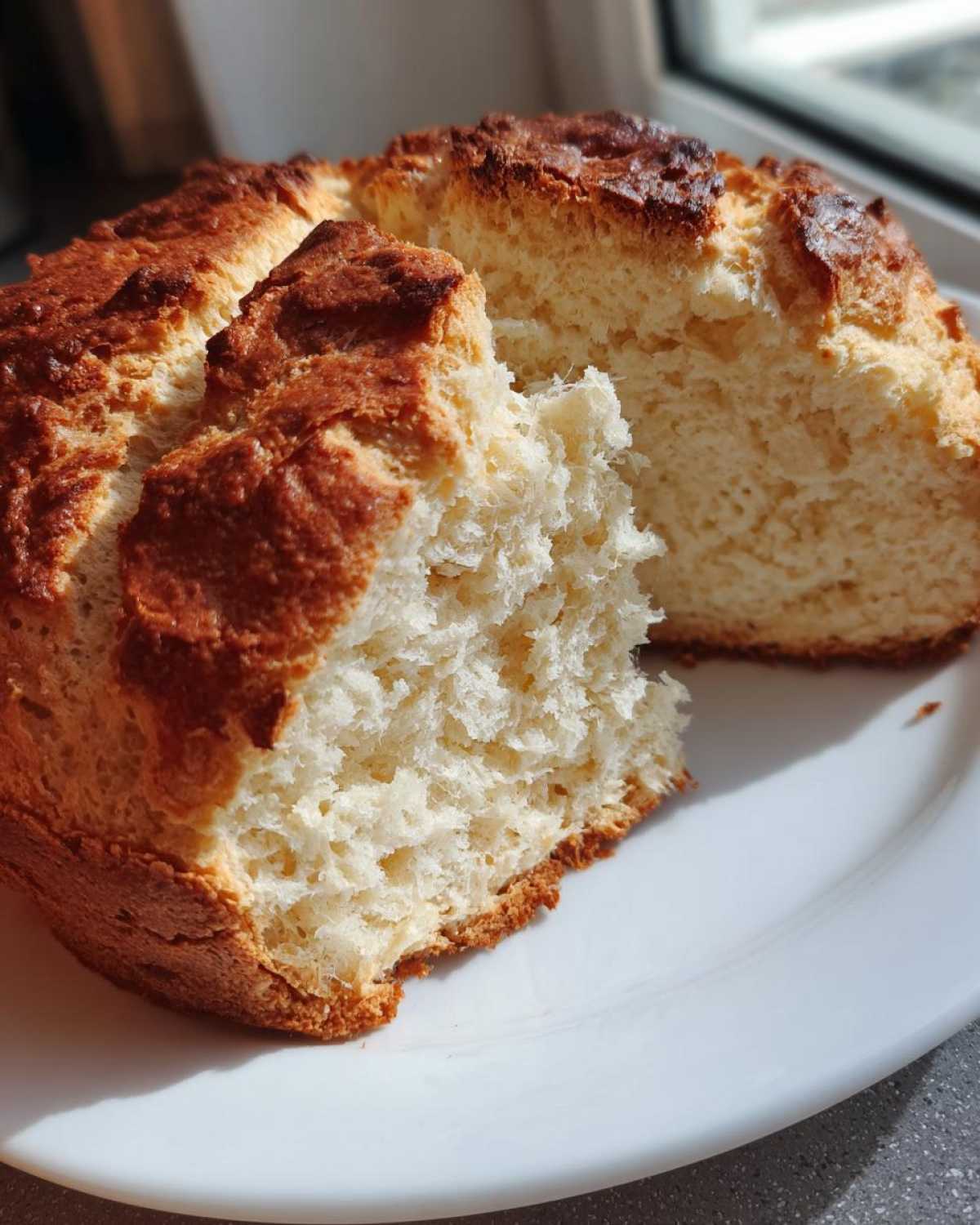 A torn half of freshly baked soda bread showing its soft, white, crumbly interior and golden-brown crust.