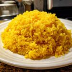 A mound of bright yellow, fluffy turmeric rice served on a white plate, ready to eat.