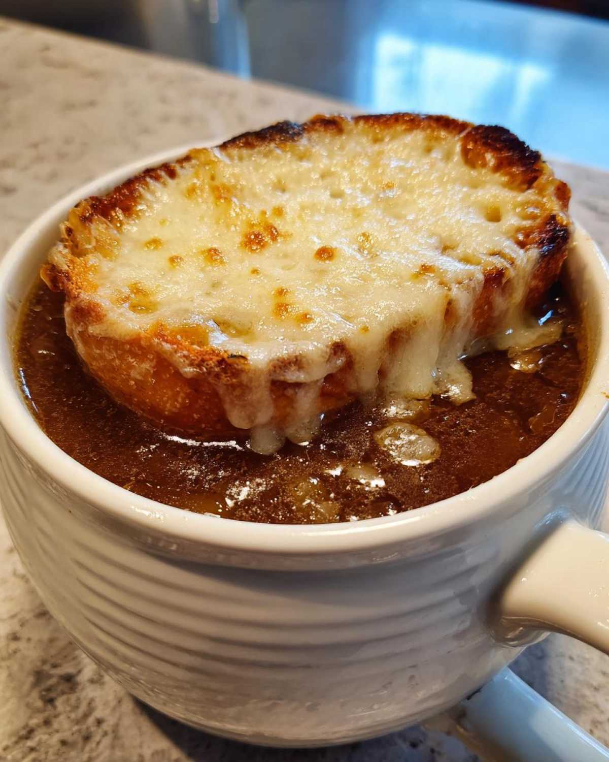 Close-up of a bowl of rich french onion soup recipe topped with a thick, melted, browned cheese layer on bread.
