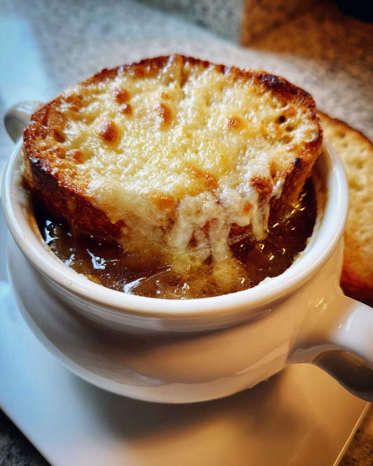 Close-up of a rich french onion soup recipe bowl topped with a thick, melted, and browned cheese crouton.