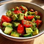 Close-up of a bowl filled with diced avocado and halved cherry tomatoes, making up the fresh avocado salad.