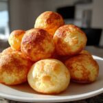 A stack of golden-brown, freshly baked brazilian cheese bread rolls piled high on a white plate.