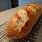 Close-up of a golden brown, crusty loaf of homemade french bread resting on a wire cooling rack.