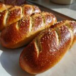 Close-up of golden brown, freshly baked pretzel dogs buns sprinkled with coarse salt on parchment paper.