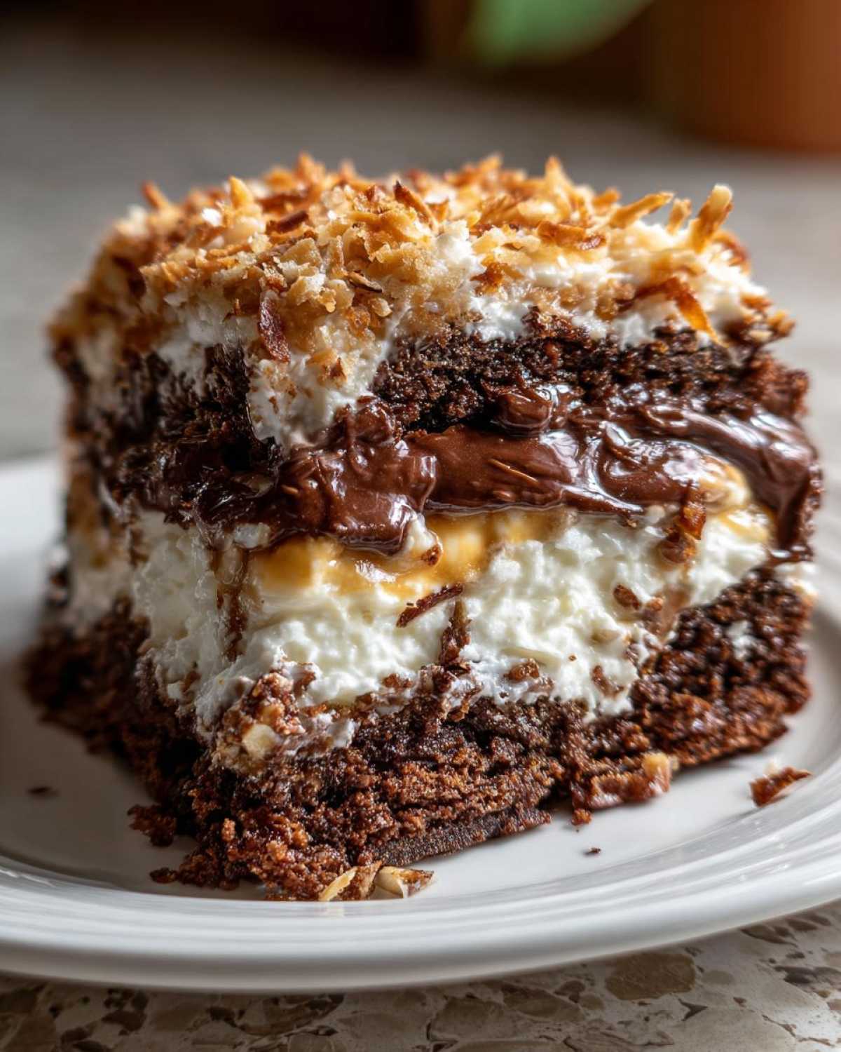 Close-up of a rich slice of german chocolate poke cake showing layers of chocolate cake, white filling, and toasted coconut topping.