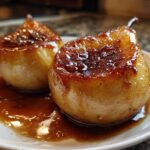 Close-up of two perfectly caramelized baked pears sitting in a rich, glossy brown sauce on a white plate.