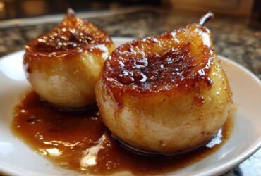Close-up of two perfectly caramelized baked pears sitting in a rich, glossy brown sauce on a white plate.