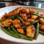Close-up of glazed, bite-sized chicken and bright green beans served together in a white bowl.