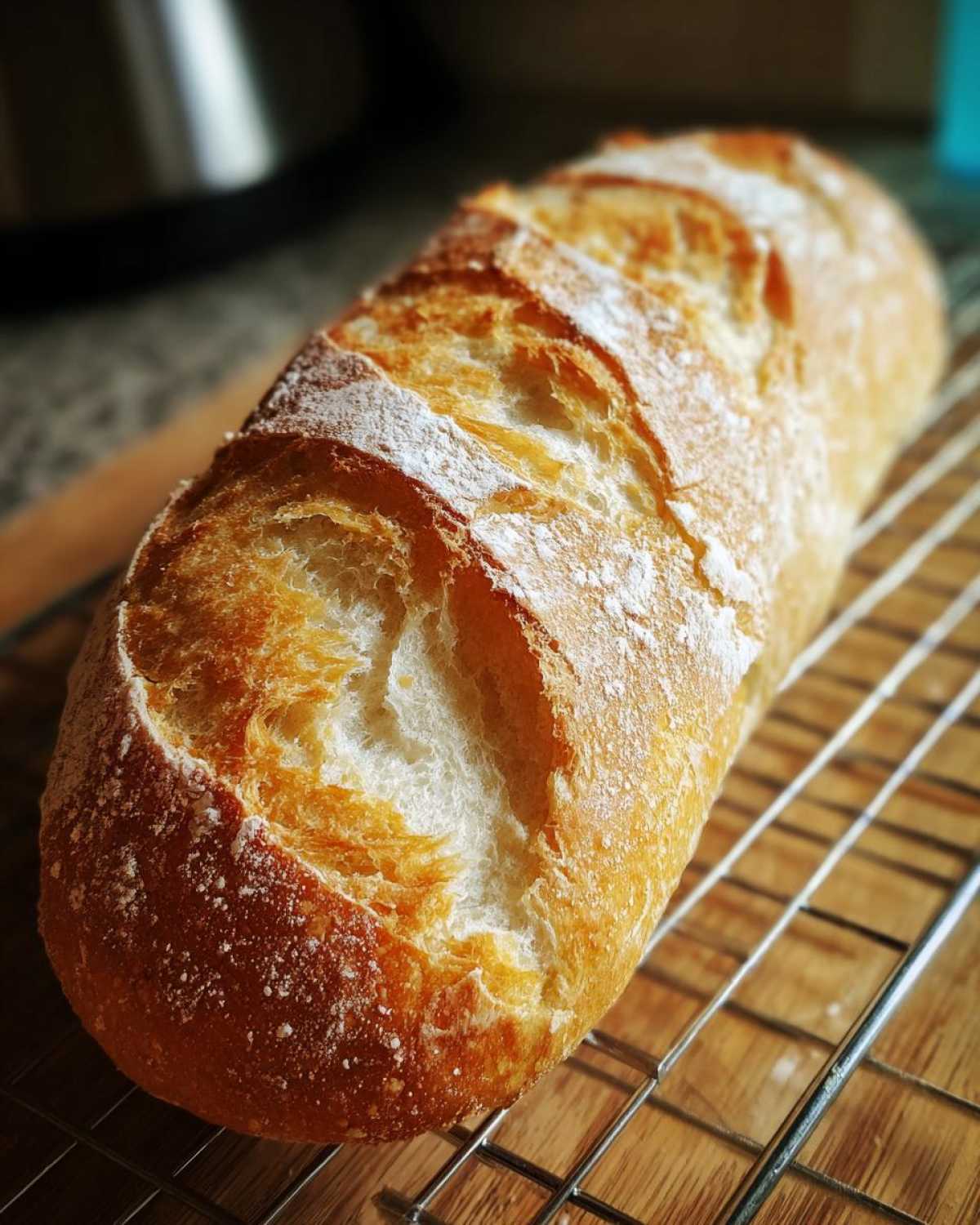 A freshly baked loaf of golden brown french bread with a crisp, scored crust resting on a wire cooling rack.