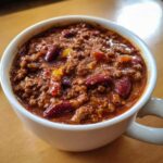 Close-up of a white mug filled with hearty, thick chili featuring ground meat and kidney beans.