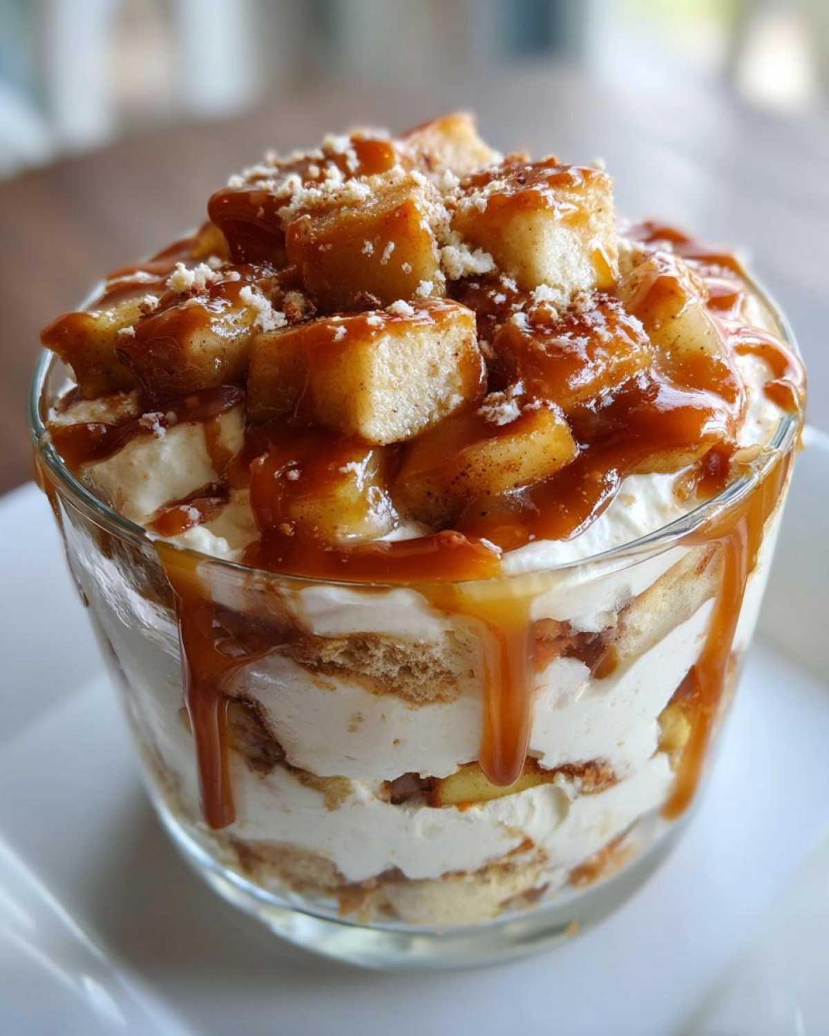 Close-up of an individual caramel apple trifle layered with cream, cake, and topped with saucy apples and nuts.