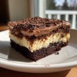 A rich slice of layered Italian love cake featuring a dark chocolate base, creamy filling, and chocolate mousse topping with shavings.