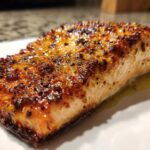 Close-up of a juicy air fryer salmon fillet with a caramelized, seasoned crust resting on a white plate.