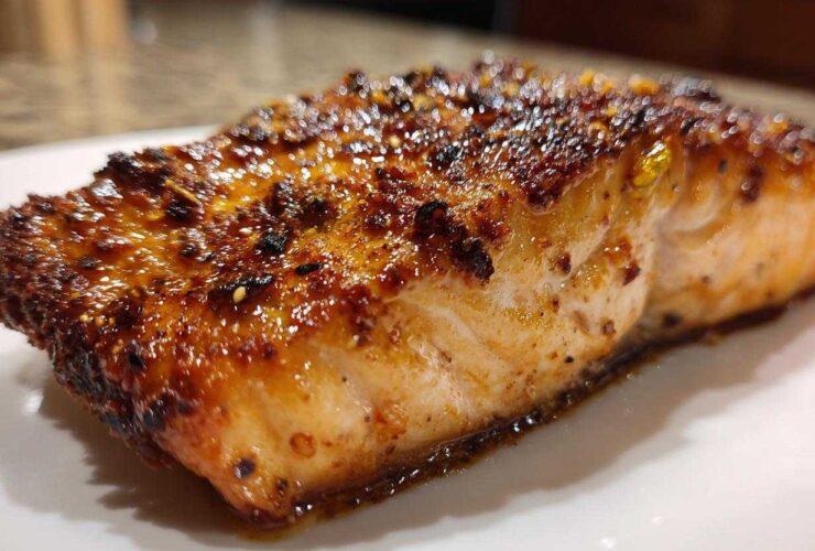 Close-up of a juicy, caramelized air fryer salmon fillet with a dark, seasoned crust resting on a white plate.