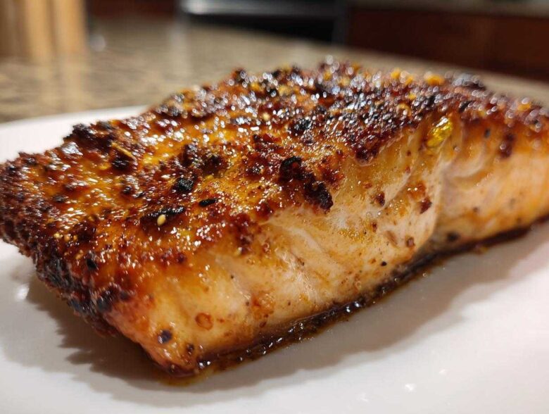 Close-up of a juicy, caramelized air fryer salmon fillet with a dark, seasoned crust resting on a white plate.