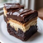 A thick slice of three-layer buckeye brownies featuring a dense brownie base, peanut butter layer, and chocolate topping.