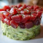 Close-up of a molded tuna tartare tower featuring bright red, diced tuna over a creamy green avocado base.