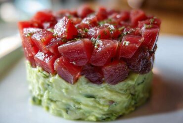 Close-up of a molded tuna tartare tower featuring bright red, diced tuna over a creamy green avocado base.