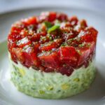 Close-up of a beautiful, layered tuna tartare stack featuring diced red ahi tuna over a creamy green avocado base.