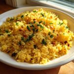 A white bowl filled with fluffy, yellow mediterranean rice, topped with chopped parsley and toasted pine nuts.