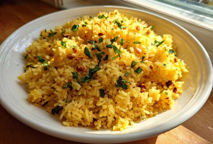 A white bowl filled with fluffy, yellow mediterranean rice, topped with chopped parsley and toasted pine nuts.