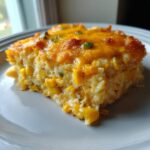 A square slice of baked Mexican corn casserole topped with melted cheddar cheese and green onions.