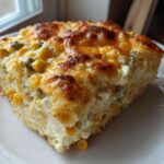 A thick, golden slice of Mexican corn casserole featuring visible kernels of corn and melted cheese topping.