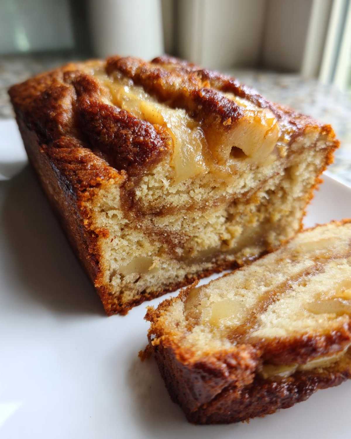 Close-up of a moist slice of apple bread showing chunks of apple and cinnamon swirl.