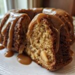 A slice cut from a moist apple bundt cake, generously topped with thick caramel sauce.