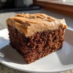 Close-up of a moist, dark slice of gingerbread cake topped with thick, light brown frosting.