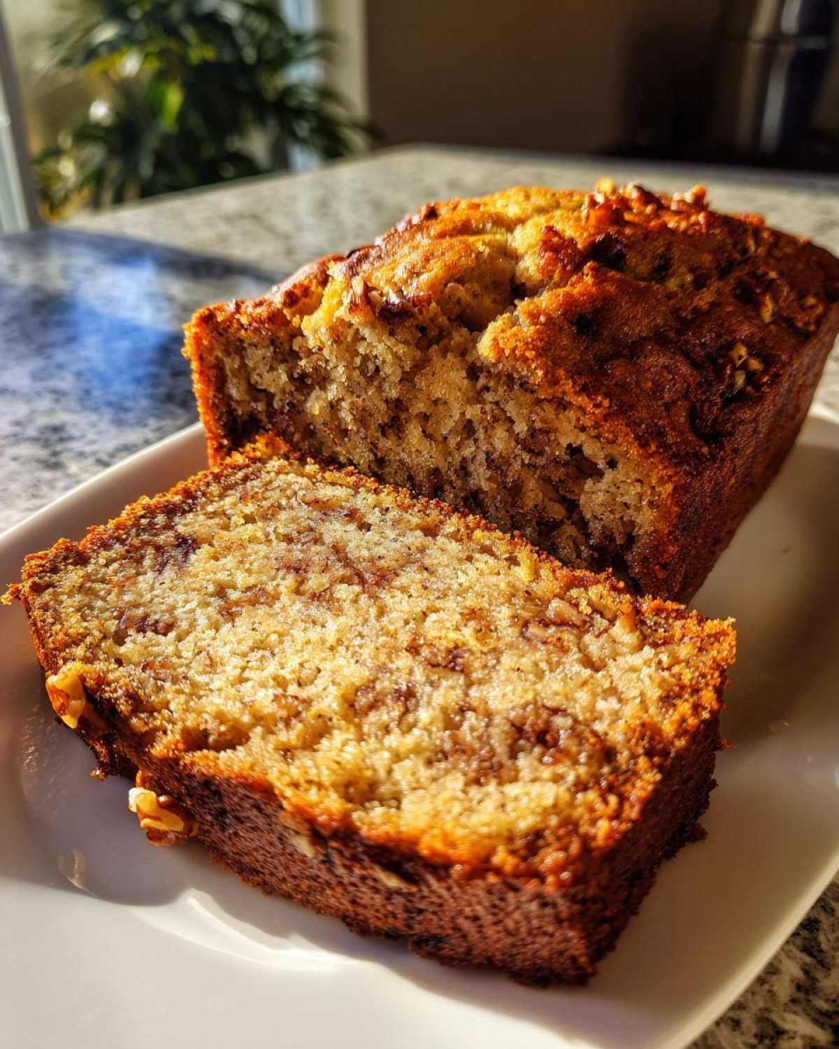 A slice of moist greek yogurt banana bread with visible walnuts, sitting next to the main loaf.