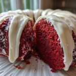 Close-up of a moist red velvet bundt cake with thick white glaze dripping down the sides.