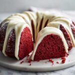 Close-up of a moist red velvet bundt cake with thick white cream cheese glaze dripping down the sides.