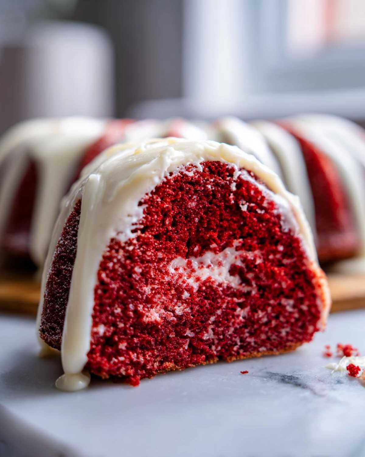 Close-up of a moist slice of red velvet bundt cake showing the vibrant red crumb and white cream cheese glaze dripping down.