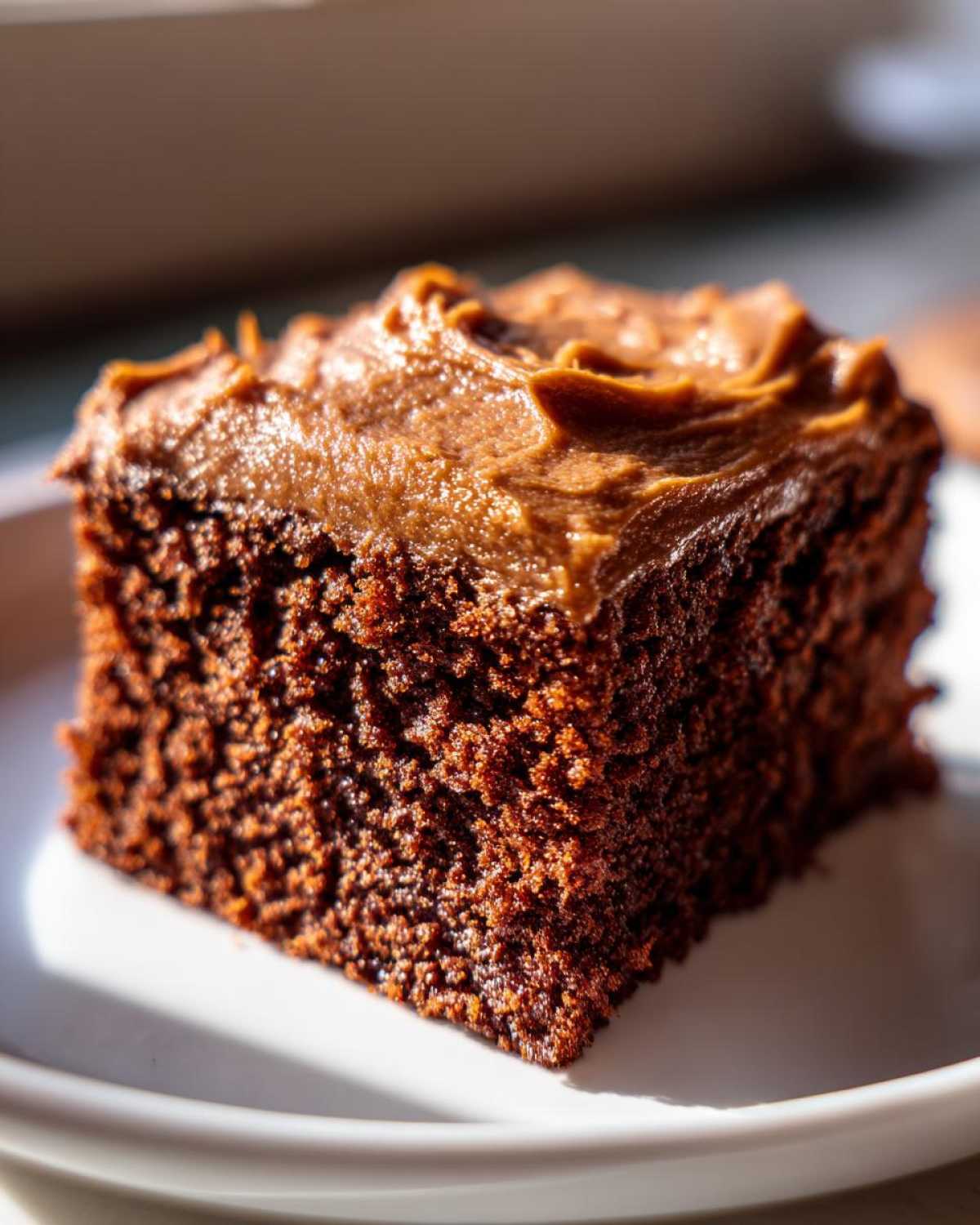 Close-up of a rich, dark slice of gingerbread cake topped with thick, swirled brown frosting.
