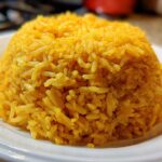 A mound of bright yellow, fluffy turmeric rice served on a white plate, ready to eat.