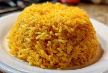 A mound of bright yellow, fluffy turmeric rice served on a white plate, ready to eat.